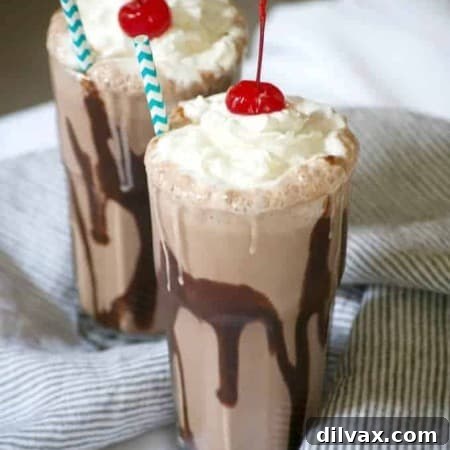 A delicious Double Chocolate Malted Milkshake in a tall glass, topped with a generous swirl of whipped cream and a bright red maraschino cherry. Chocolate syrup drips down the inside of the glass, emphasizing its rich flavor.