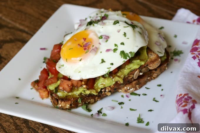 Delicious Bruschetta Fried Egg Avocado Toast with whole grain bread, smashed avocado, marinated tomato and a fried egg, perfect for a great start to your day!