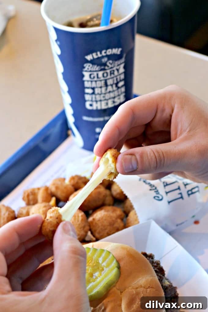 National Cheese Curd Day: Celebrate at Culver's 6 A hand holding a perfectly stretched cheese curd, highlighting the melted cheese pull against a blurred background