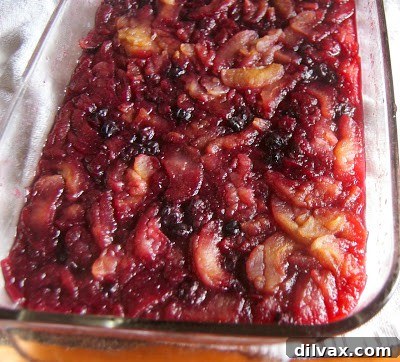 A rustic wooden spoon resting in a bowl of baked blueberry applesauce.