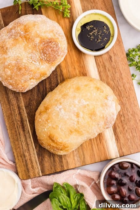 Two beautiful Ciabatta loaves on a wooden cutting board, with a bowl of olive oil for dipping.