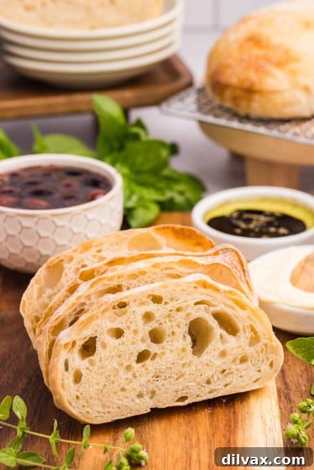 Slices of Ciabatta bread on a cutting board, accompanied by a bowl of dipping sauce and olives.