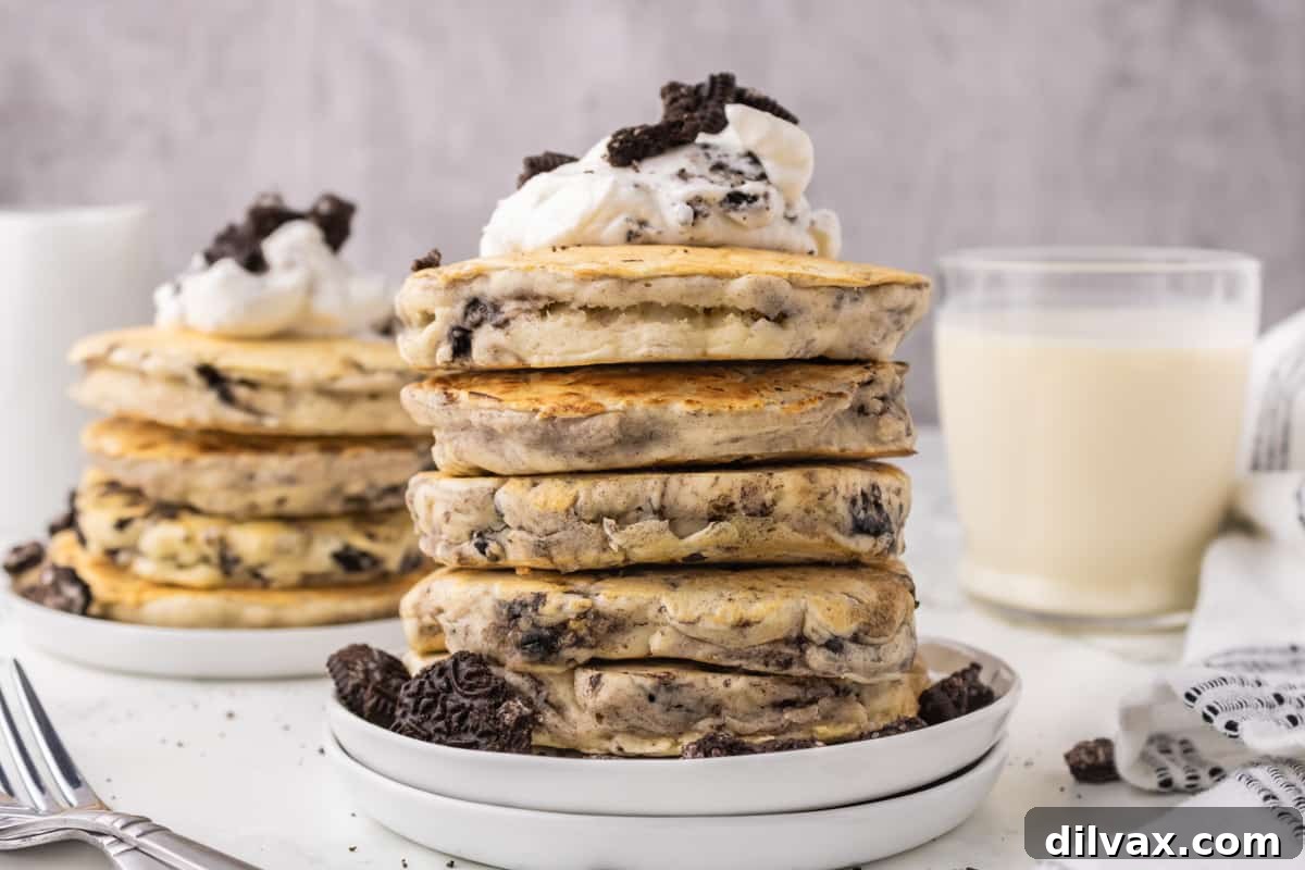 A tall stack of fluffy Oreo pancakes topped with whipped cream and a whole Oreo cookie.