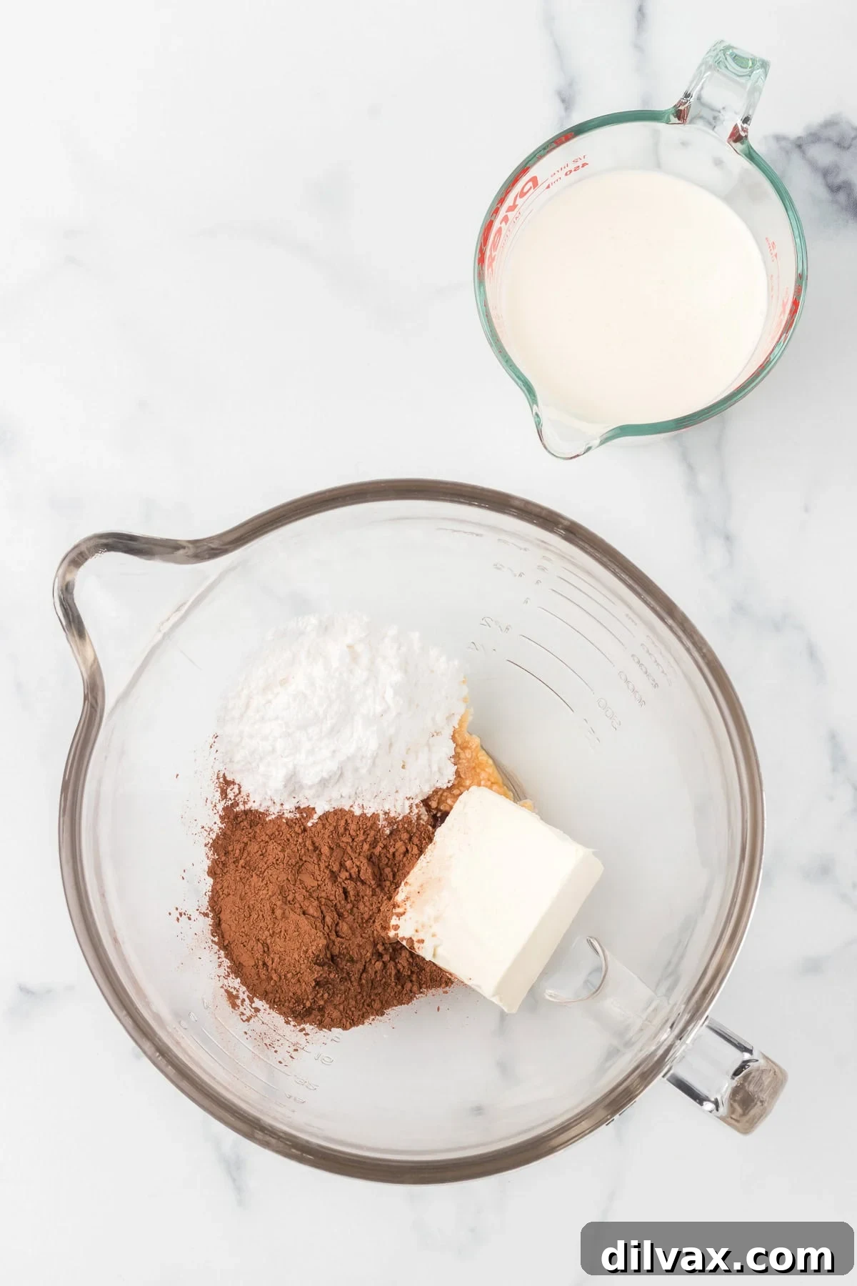 Ingredients for a Chocolate Cool Whip substitute in a mixing bowl next to a cup of heavy cream.