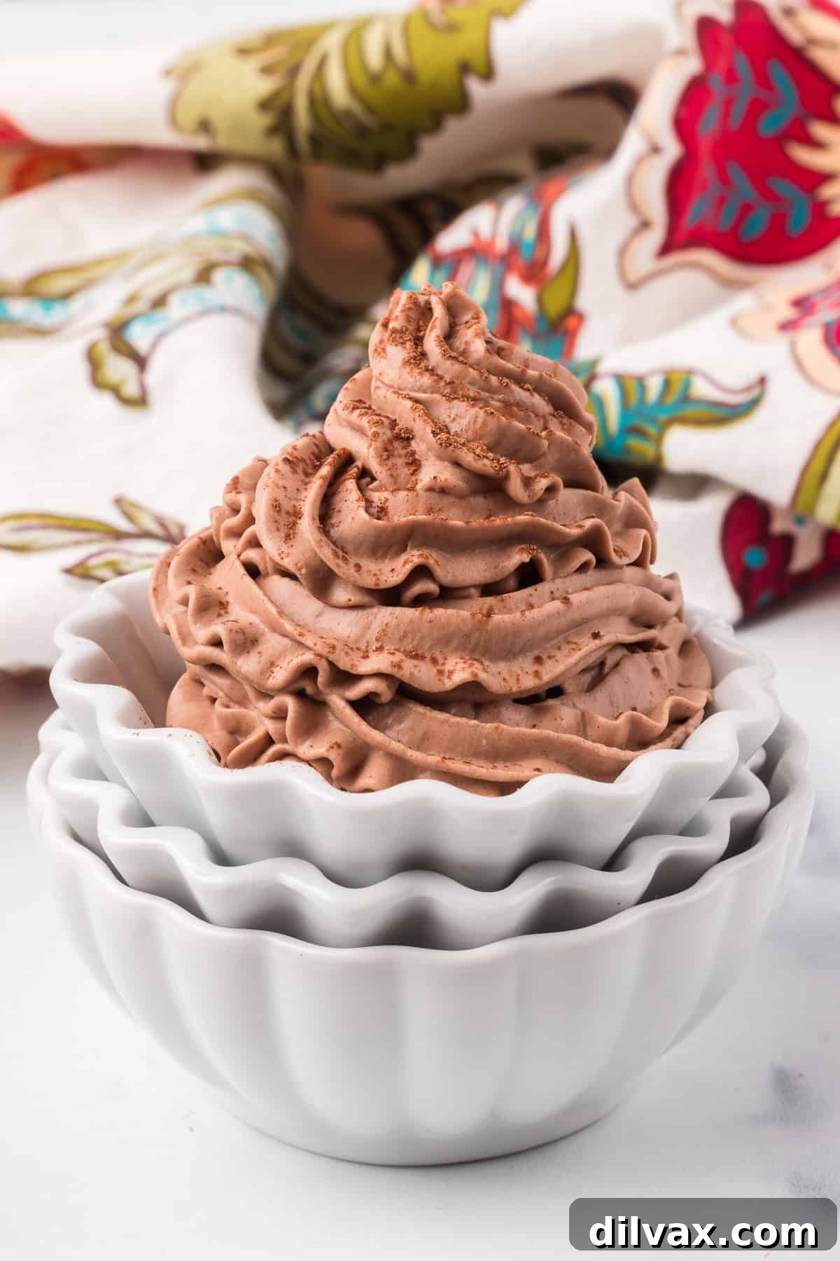 A piping of stabilized whipped cream made with chocolate cocoa in bowls in front of a brightly colored floral napkin.