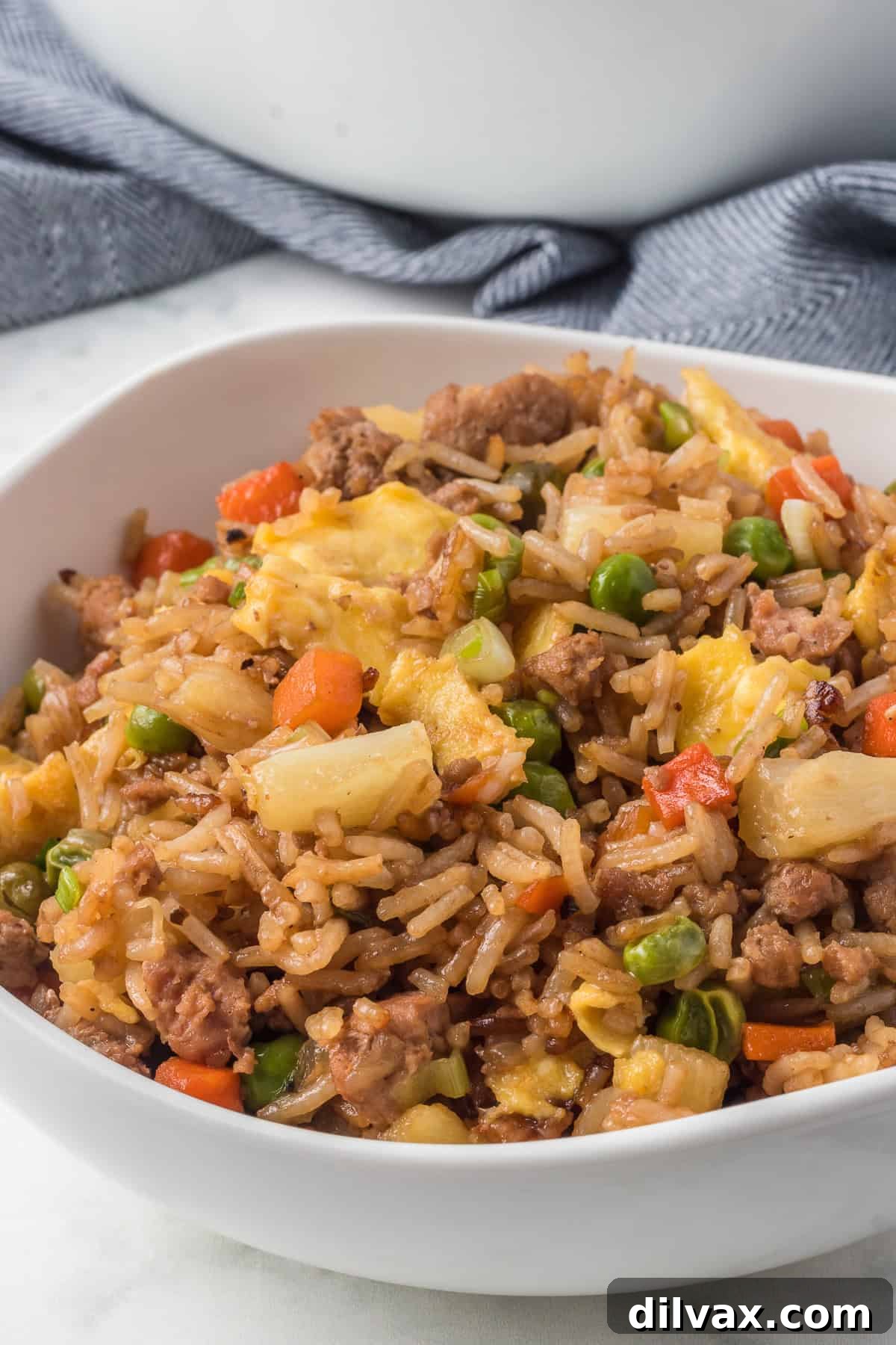 Rice, pineapple, ground pork, carrots, peas, and egg in a bowl.